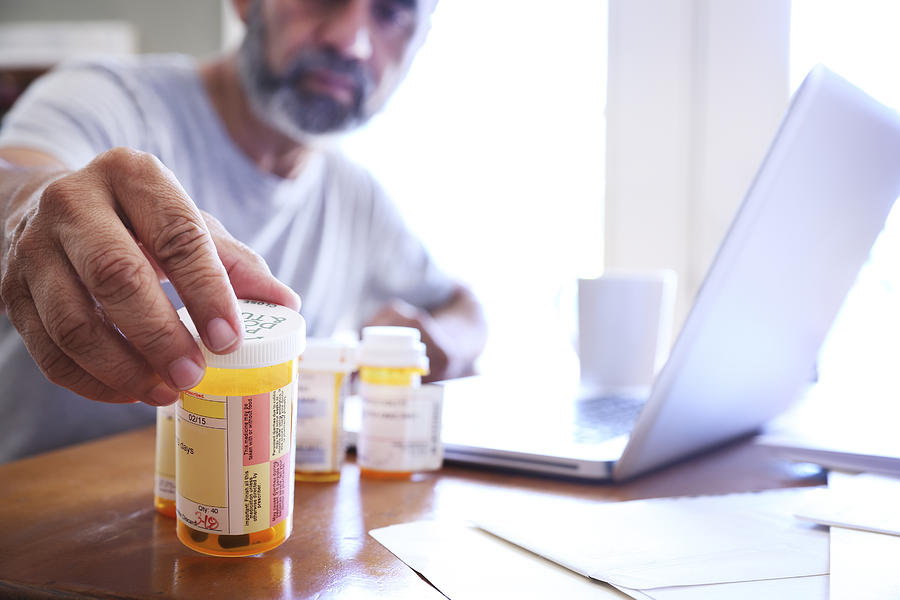 Hispanic Man Sitting At Dining Room Table Reaches For His Prescription Medications Photograph by Dny59