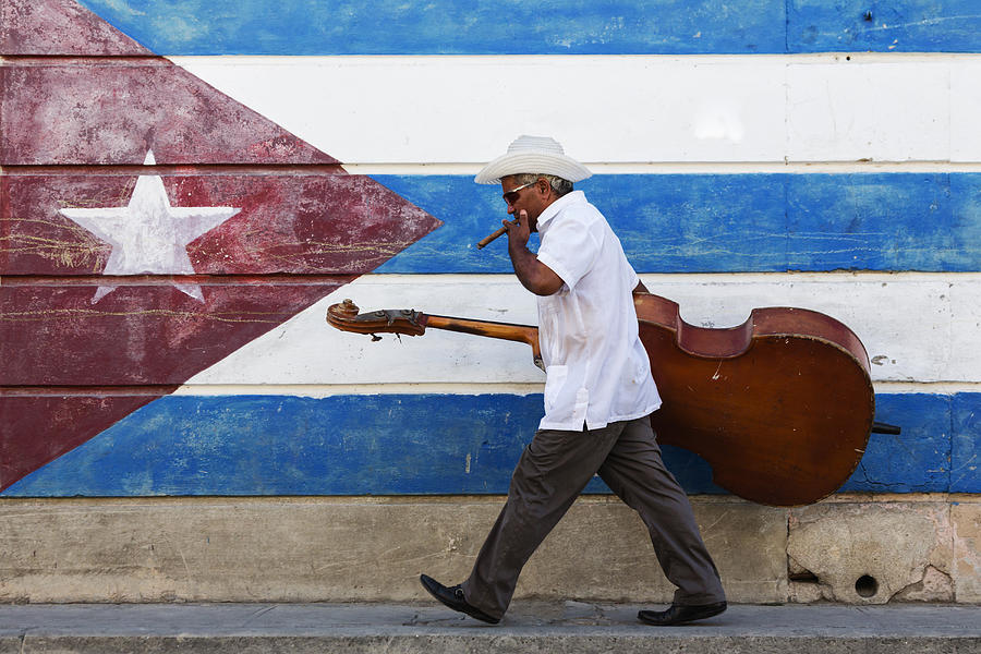 Hispanic musician carrying upright bass in front of Cuban flag mural Photograph by Pixelchrome Inc