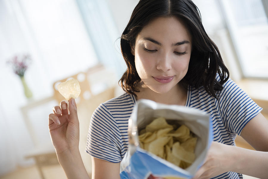 Hispanic woman reading ingredients on bag of potato chips Photograph by JGI/Jamie Grill
