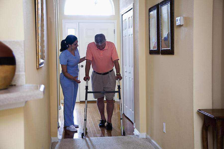 Home health aide with senior man using walker Photograph by Kali9