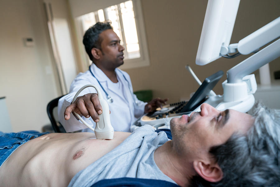 Indian doctor doing a heart ultrasound to a middle aged male patient Photograph by Andresr
