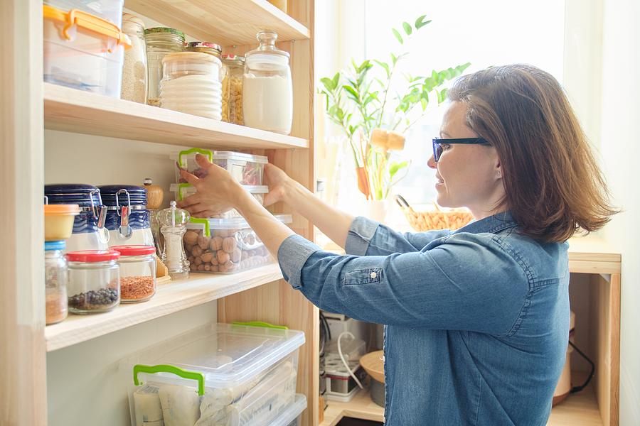 Interior of wooden pantry with products for cooking. Adult woman taking kitchenware and food from the shelves Photograph by Valeriy_G