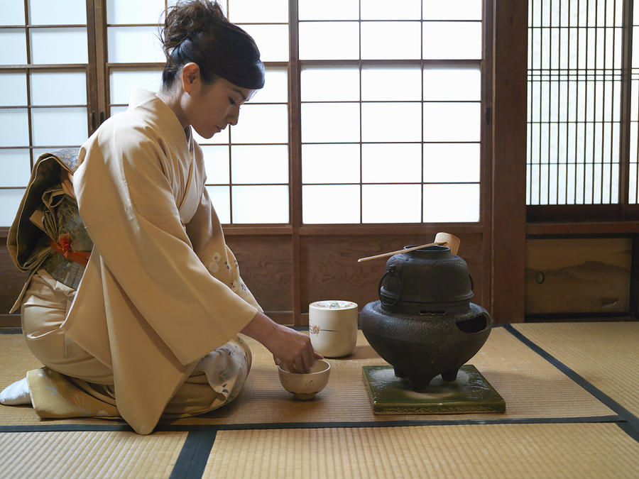 Japan, Tokyo, woman kneeling on floor, preparing tea, side view Photograph by Michael H