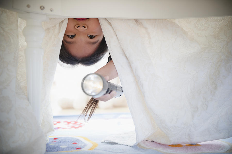 Korean girl looking under bed with flashlight Photograph by Blend Images - JGI/Jamie Grill