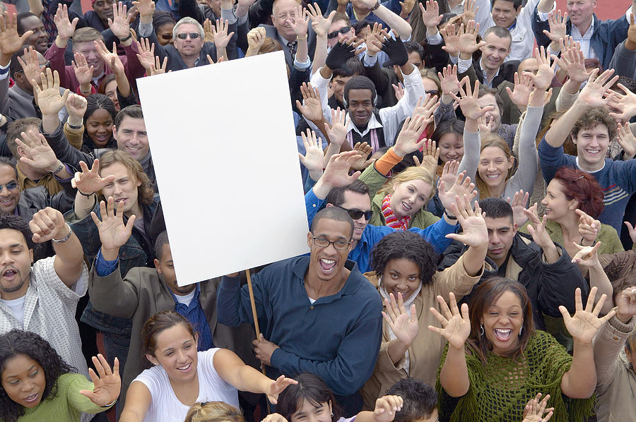 Large Crowd of People with Their Hands Raised in the Air with One Man Holding a Blank Placard Photograph by Digital Vision.