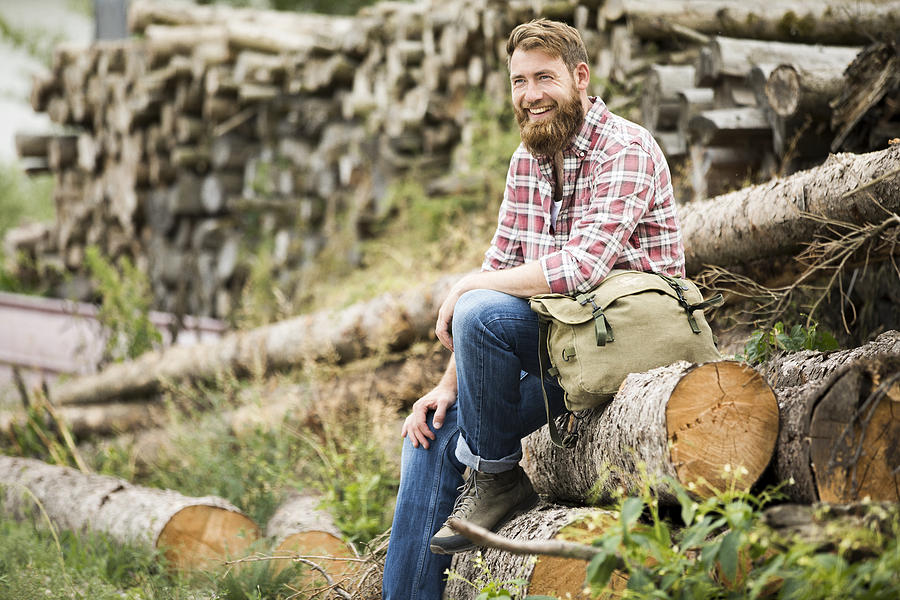 Laughing bearded man sitting on stack of wood Photograph by Westend61