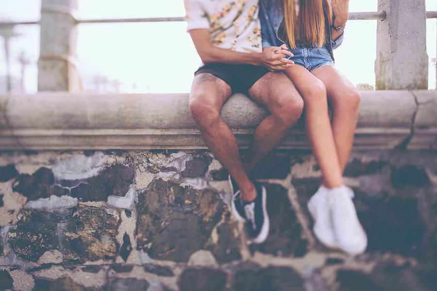 Legs of hipster couple sitting on a wall holding hands Photograph by Wundervisuals
