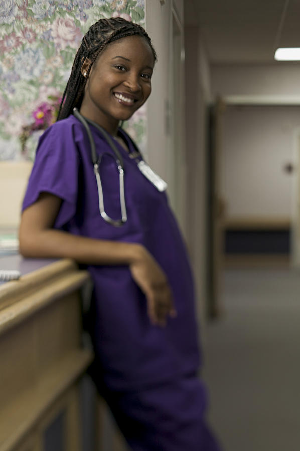 Lifestyle Shot Of A Young Adult Female Nurse With Purple Scrubs In A Hospital Hallway As She Smiles Photograph by Photodisc
