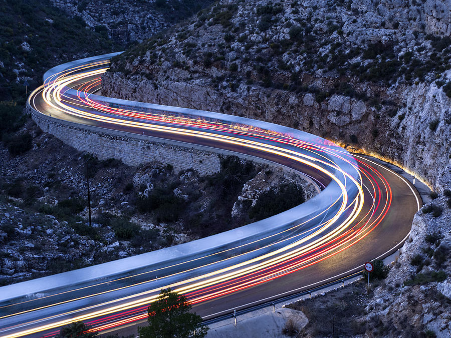 Lights and trails of vehicles, cars and trucks, circulating along a road of mountain between ravines with circular curves closed in the nightfall. Photograph by Jose A. Bernat Bacete