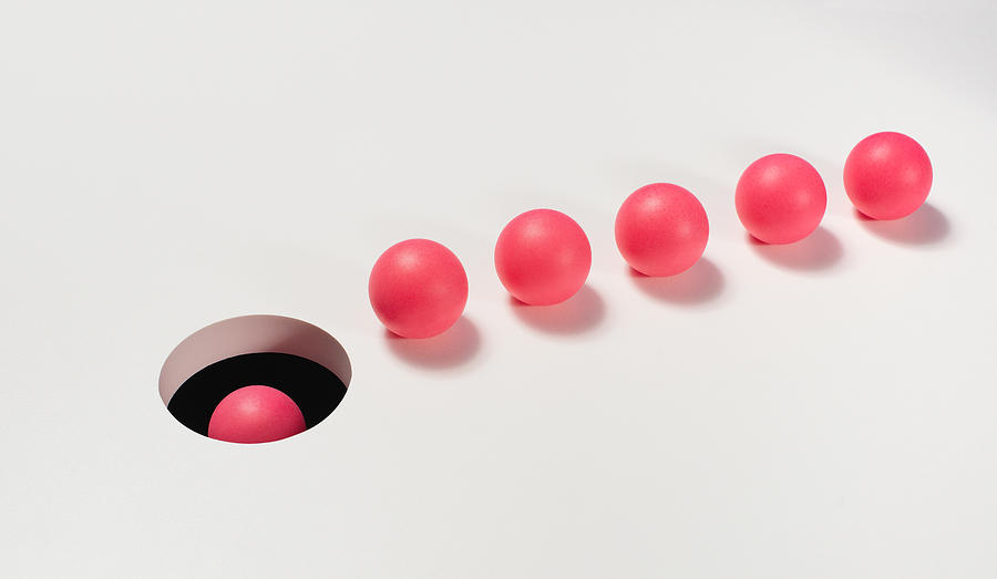 Line of red balls heading towards a hole Photograph by PM Images
