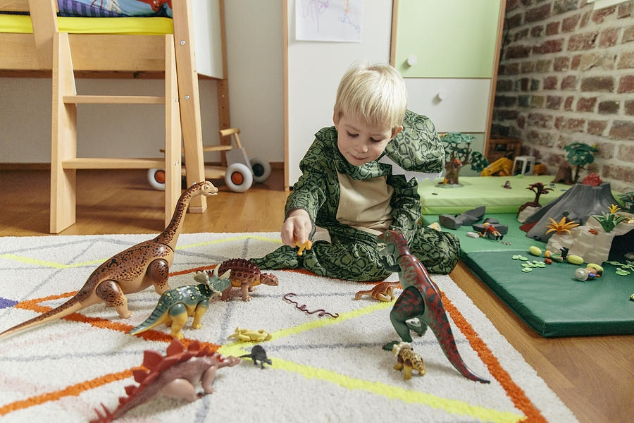Little boy wearing dinosaur costume playing with toy dinosaurs Photograph by Westend61