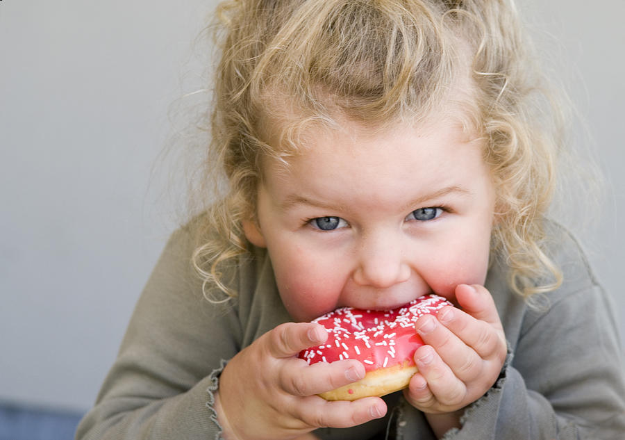 Little girl eating jelly-glazed donut with sprinkles Photograph by LisaValder
