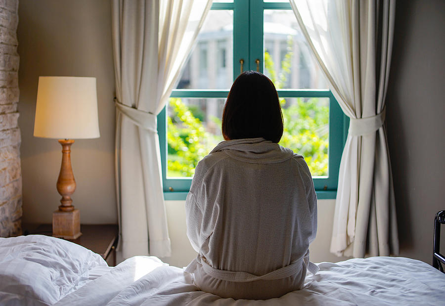 Lone woman sitting on the bed looking out at the window in the morning Photograph by Sorajack
