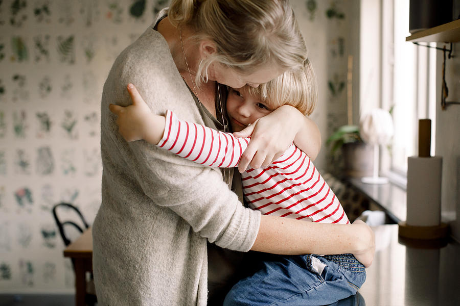 Loving daughter embracing mother while sitting on kitchen counter at home Photograph by Maskot