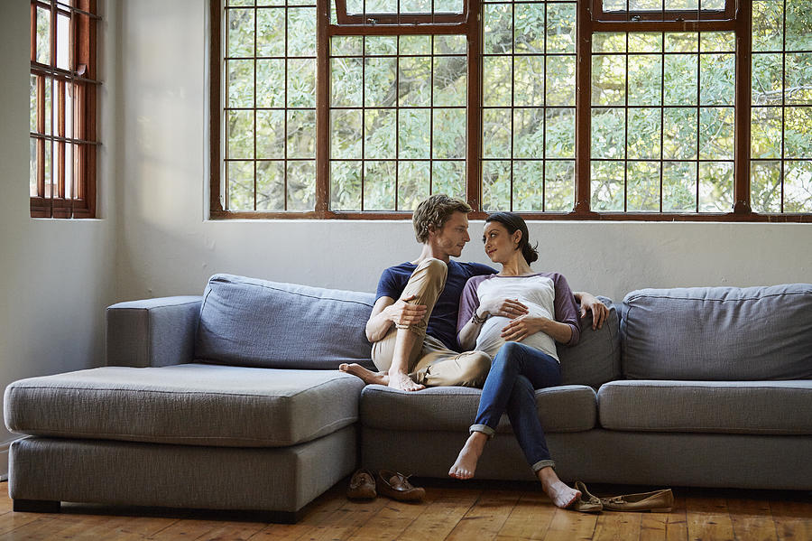 Loving expectant couple sitting on sofa at home Photograph by Morsa Images