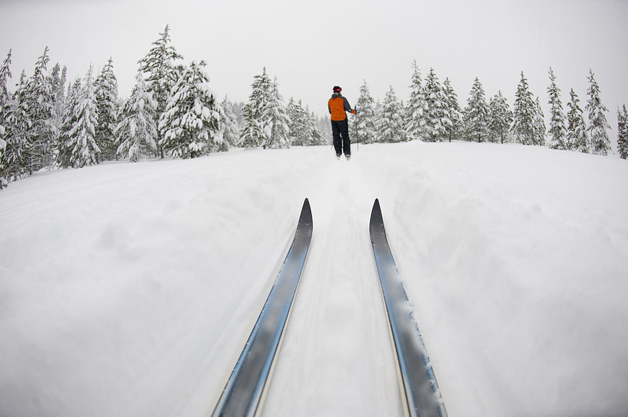 Low angle view of cross country ski tips and one young woman Nordic skiing on a cross country trial in the snow in Bend, Oregon. Photograph by Jonathan Kingston