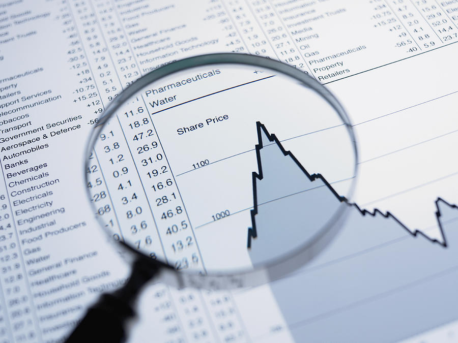 Magnifying glass and descending line graph and list of share prices Photograph by Adam Gault