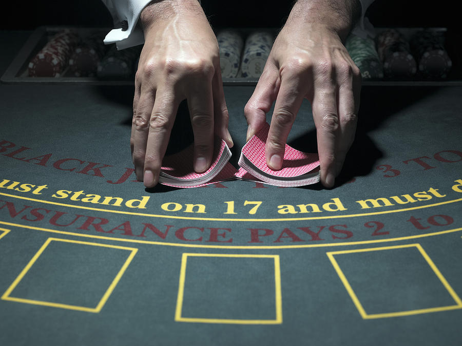 Male croupier shuffling cards at table, merging two piles, close-up Photograph by John Howard