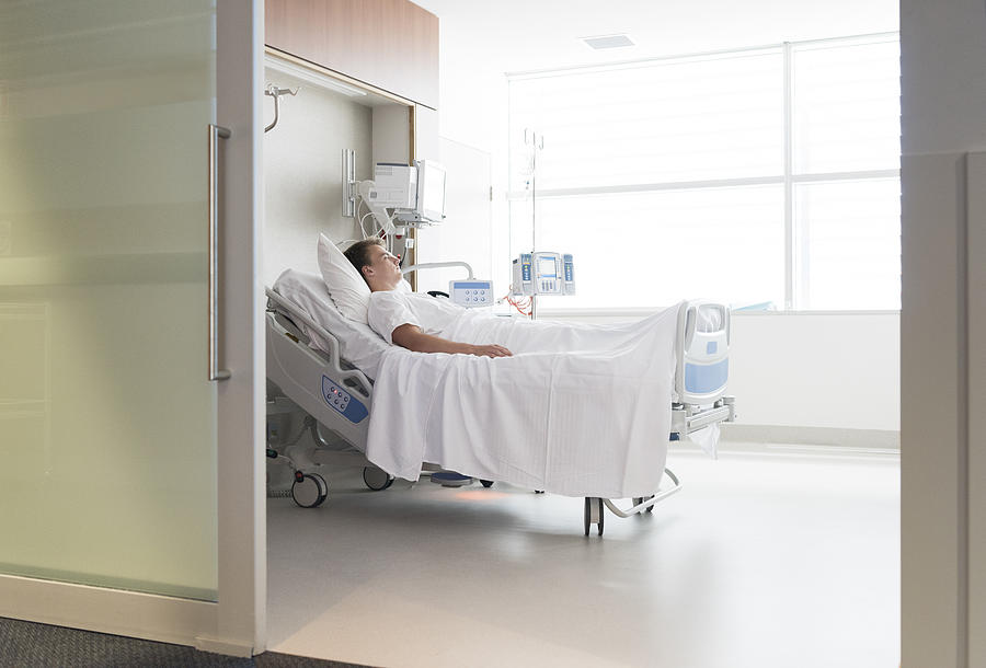 Male patient lying in hospital bed, view through doorway Photograph by JohnnyGreig