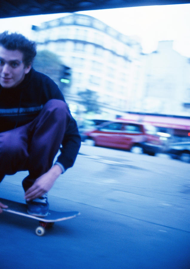 Male teenager squatting on moving skateboard, close-up Photograph by Patrick Sheandell OCarroll