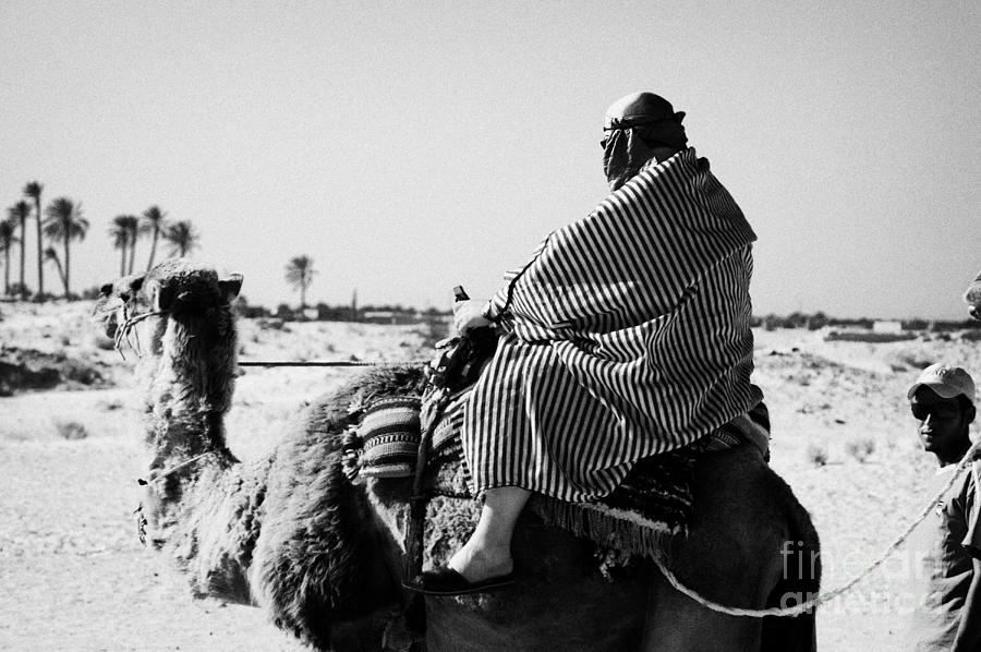 bedouin guide in modern clothing leads british tourists riding camels and  wearing desert clothes into the sahara desert at Douz Tunisia Greeting Card  by Joe Fox