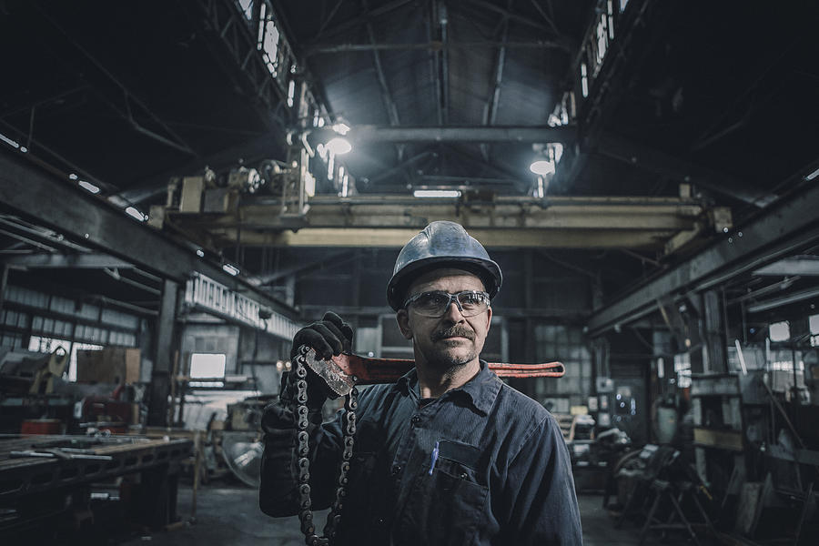 Male worker carrying work tool looking away while standing in factory Photograph by Cavan Images