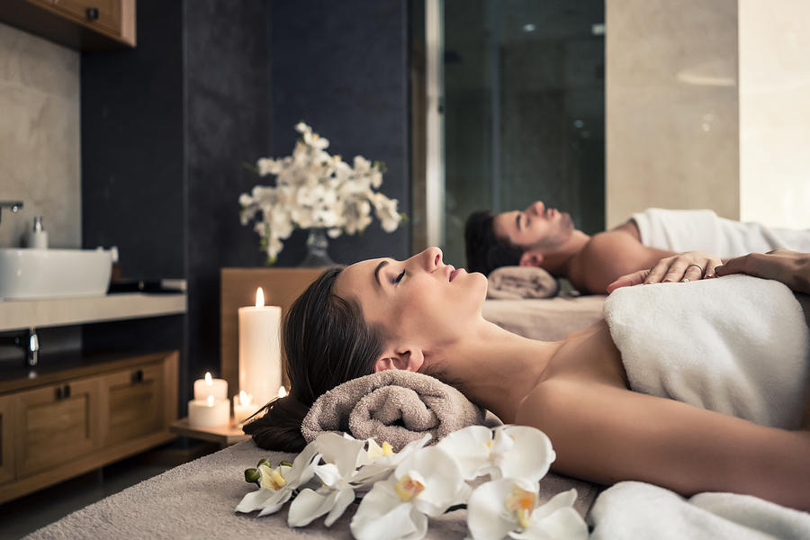 Man and woman lying down on massage beds at Asian wellness center Photograph by Kzenon