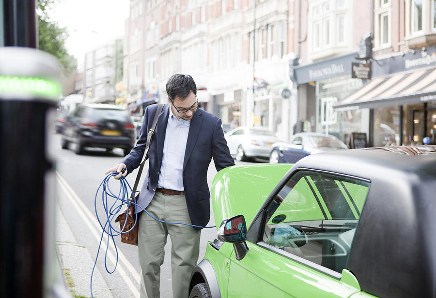 Man charging electric car on street Photograph by Nancy Honey
