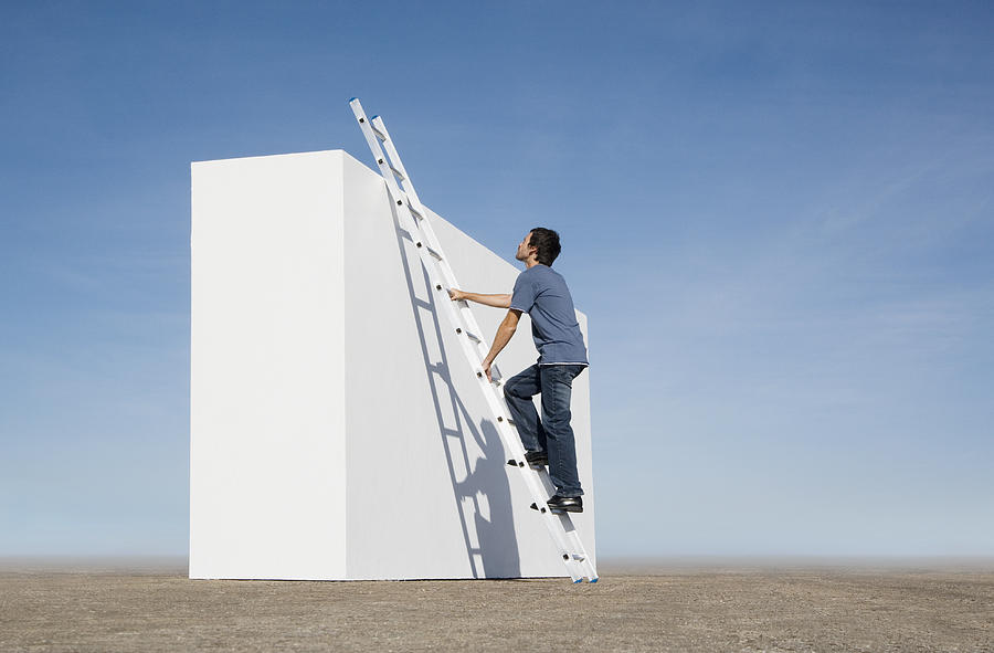 Man climbing ladder against wall outdoors Photograph by Martin Barraud