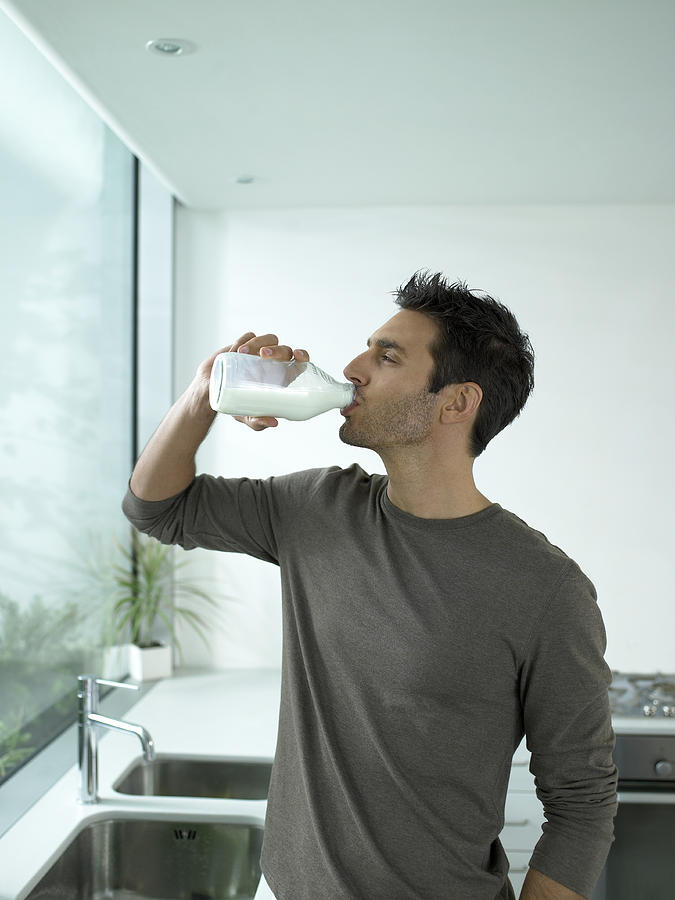 Man drinking bottle of milk in kitchen Photograph by Michael Blann
