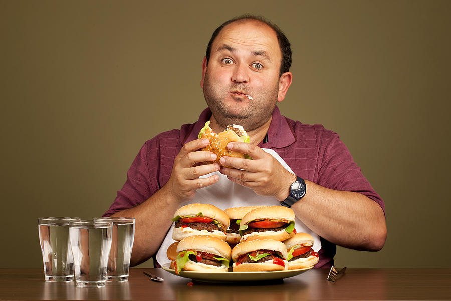 Man eating many burgers Photograph by MediaProduction