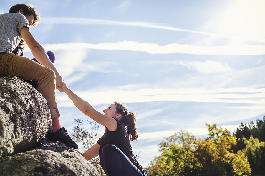 Man helping female friend to climb rock Photograph by Morsa Images