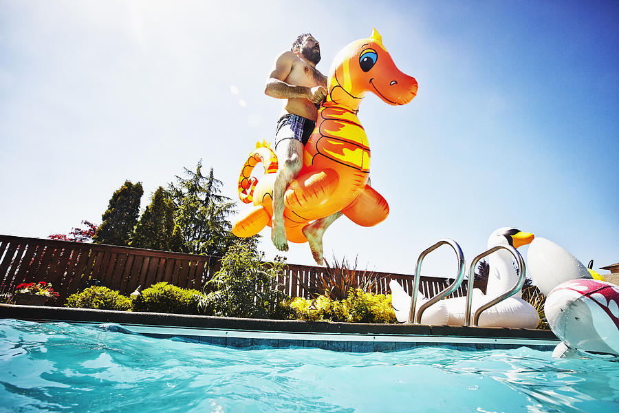 Man jumping into pool with inflatable pool toy Photograph by Thomas Barwick