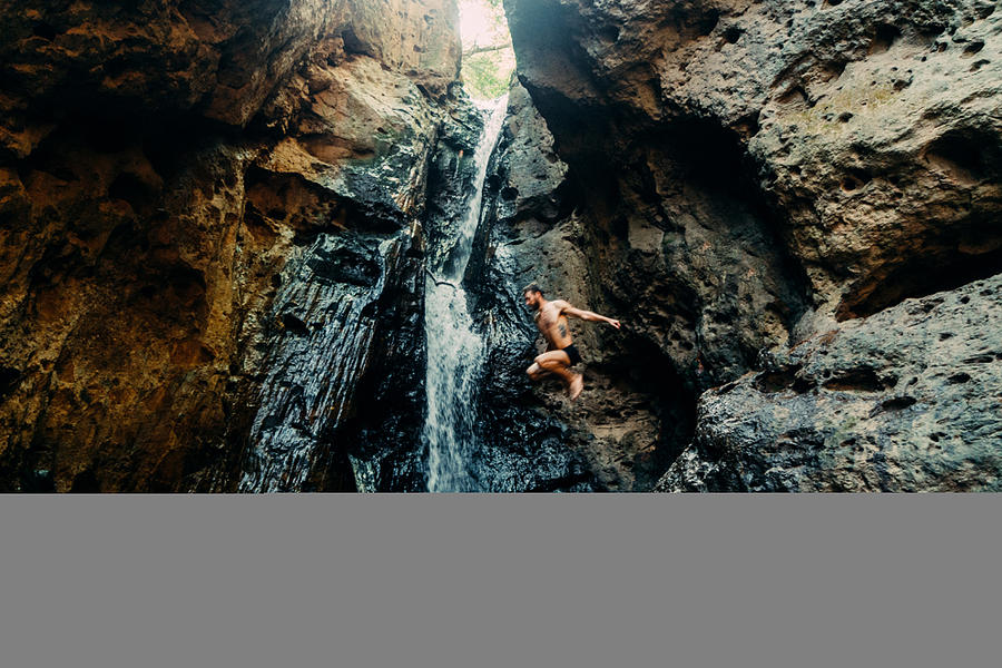 Man jumping into tropical waterfall Photograph by Oleh_Slobodeniuk