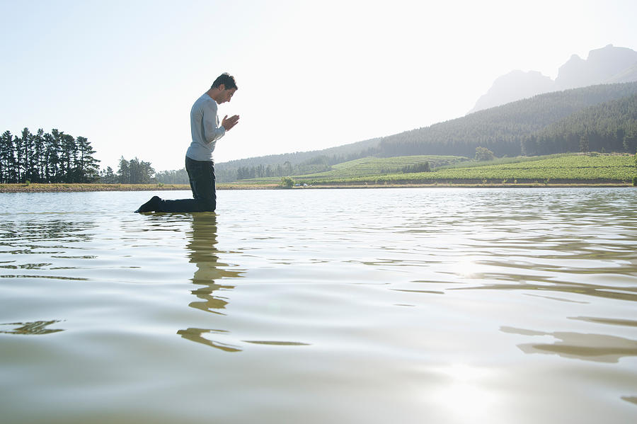 Man kneeling on water praying Photograph by Martin Barraud