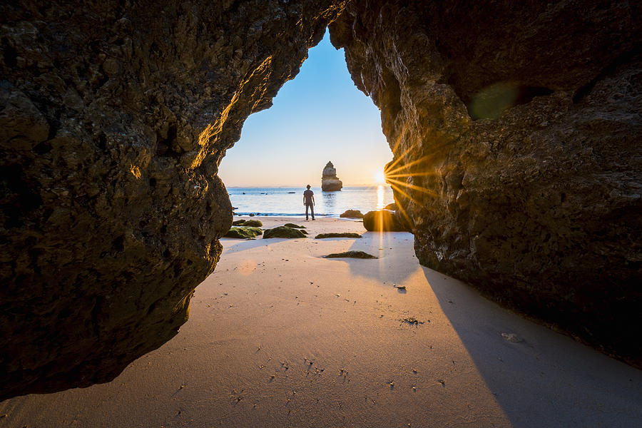 Man looking at view on the beach at sunrise, Algarve, Portugal Photograph by © Marco Bottigelli