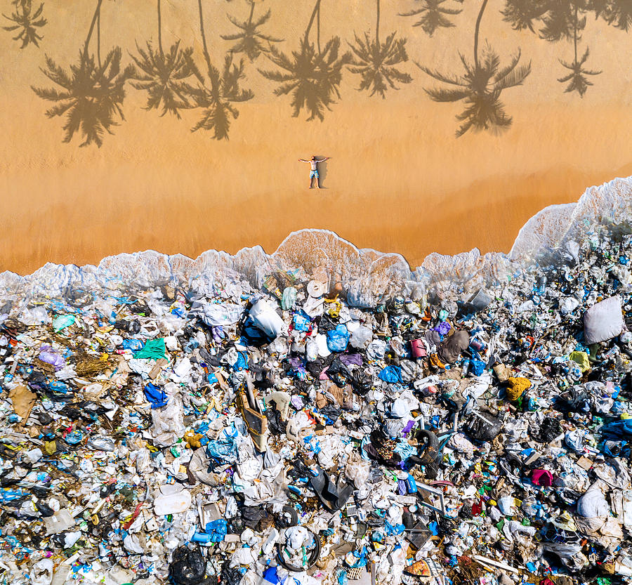 Man lying on the beach with garbage in the water. Ocean pollution concept with plastic and garbage Photograph by Anton Petrus