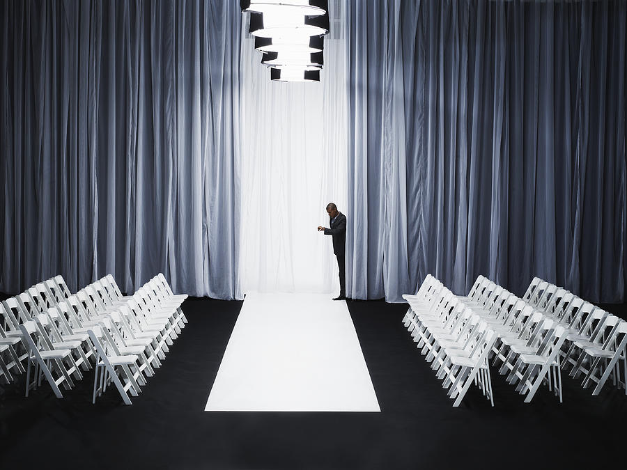 Man peeking out from behind curtain on catwalk, checking watch Photograph by Thomas Barwick