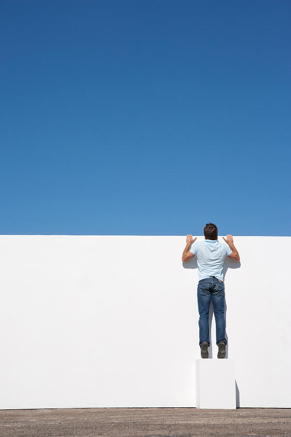 Man peering over wall outdoors with blue sky Photograph by Martin Barraud