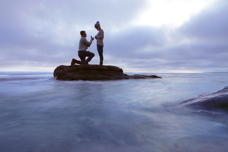 Man proposing to woman on rock in sea Photograph by Peter Cade