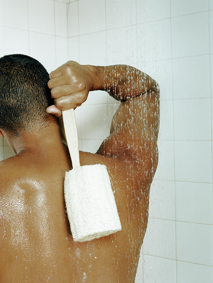 Man scrubbing back with loofah in shower, rear view Photograph by Pnc