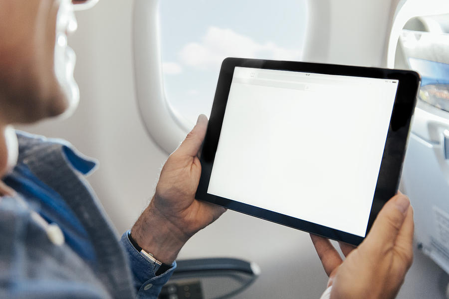 Man sitting on an airplane holding digital tablet Photograph by Westend61