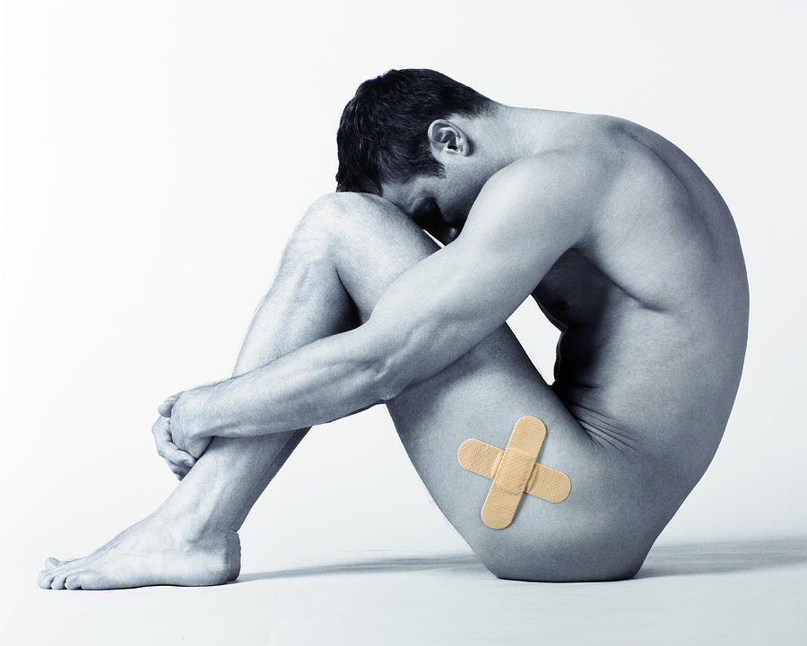 Man sitting on floor, bandages forming cross-shape on side of leg Photograph by Adam Gault