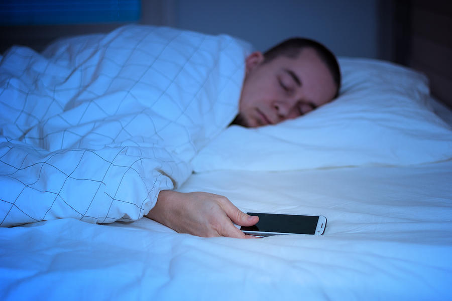 Man sleeping in bed and holding a mobile phone Photograph by Tuomas Lehtinen