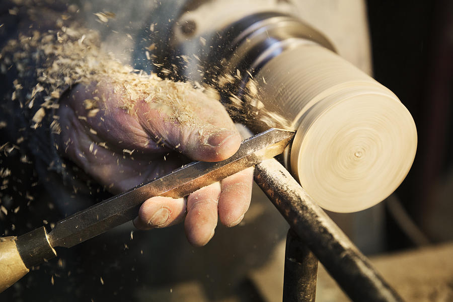 Man standing at a woodworking machine in a carpentry workshop, turning a piece of wood. Photograph by Mint Images