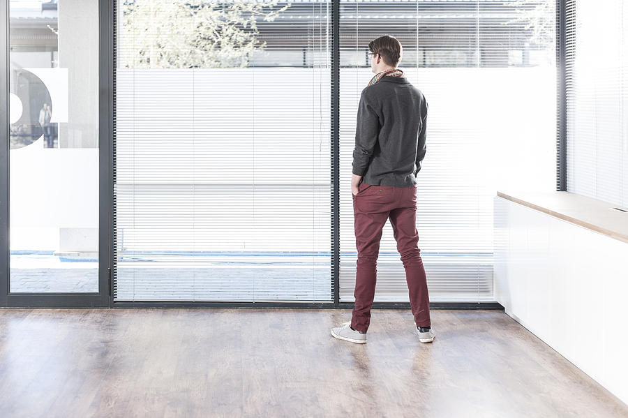Man standing in empty office looking out of window Photograph by Westend61
