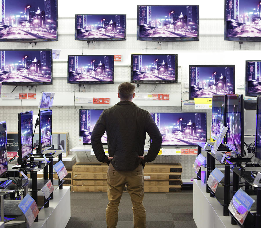Man stood in shop surrounded by televisions Photograph by Peter Cade