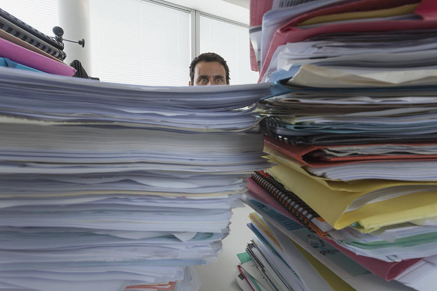 Man surrounded by piles of files in office Photograph by Paul Harizan