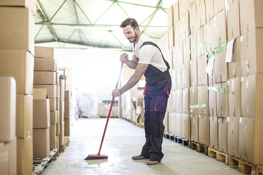 Man sweeping the warehouse floor Photograph by GoodLifeStudio