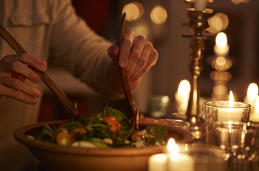 Man taking salad from bowl at candlelight dinner Photograph by Klaus Vedfelt